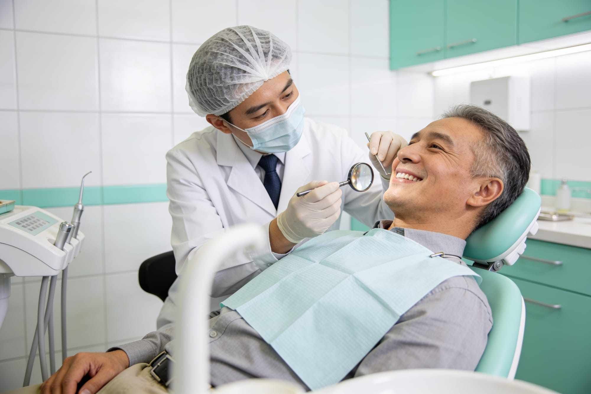 A dentist gently examining a smiling patient in the chair with a small mirror