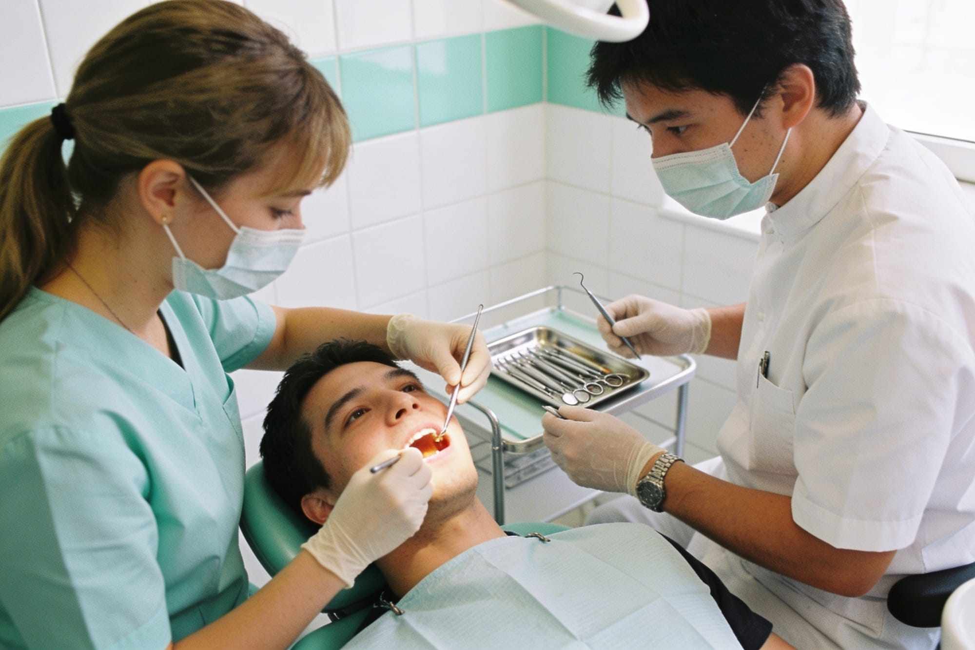 A dentist and a nurse preparing a tidy instrument tray next to a patient