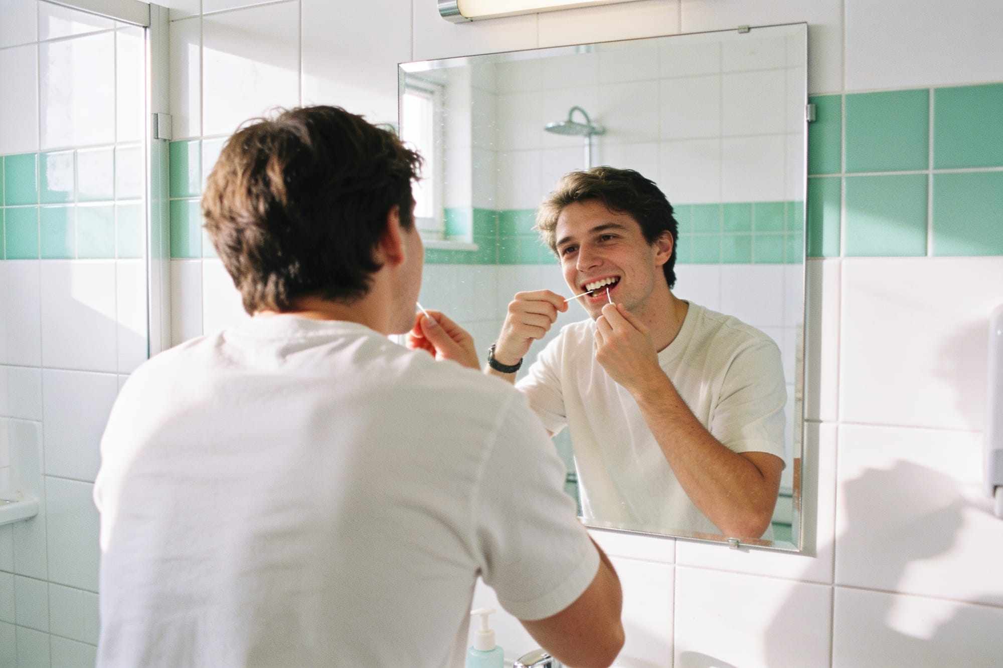 A person flossing their teeth in front of a bathroom mirror